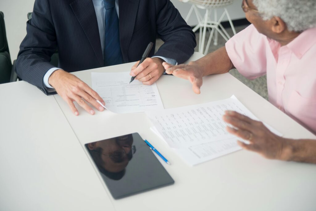 A business meeting between an elderly client and a accountant discussing documents at an office table.